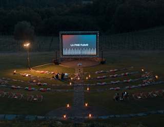 Lanterns light a path through the amphitheatre to a large screen set up for an outdoor movie experience, seen from above.