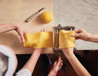 Birds-eye-view of hands passing pasta through a pasta machine