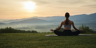 Lady in a lotus yoga pose on a lawn with views of sunrise over the Tuscan hills