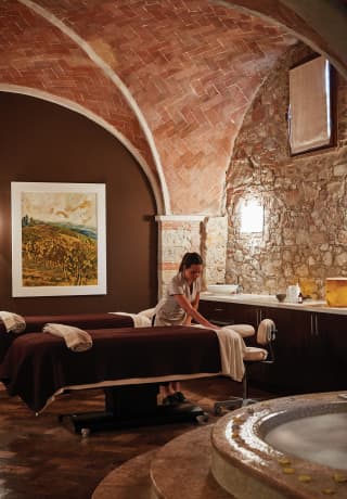 Spa therapist preparing a massage table in a lamplit, vaulted spa area>