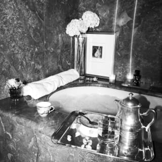 A relaxing bath full of bubbles awaits, with flowers and lit candles on its marble-topped edges, and a silver tray of supper