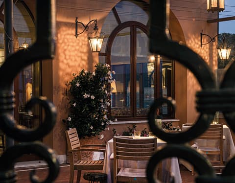 Glass lanterns throw golden patterns onto the pink hotel walls at dusk. The restaurant terrace appears through ornate ironwork
