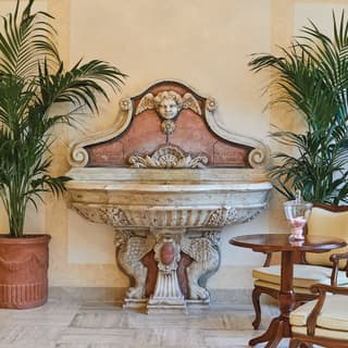 Ornate baroque indoor fountain surrounded by potted palm plants