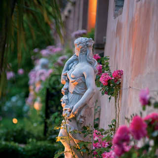 Close-up of a Venus statuette surrounded by pink flowers in a lamplit garden