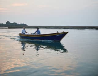 Two men explore the outer edges of the lagoon at dusk, steering a small motorboat through the water