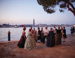 A waiter in a traditional gondolier costume carries drinks through an 18th Century themed masquerade ball on the waterfront