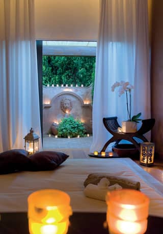 Candlelit spa treatment room with open patio doors leading to a courtyard beyond>