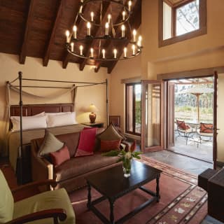 Spacious garden-view room with four-poster bed looking through open doors to a sunny terrace with rural views