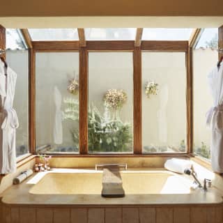 Enormous bath tucked into a glass-panelled nook with bathrobes hanging either side