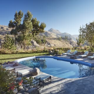 Oval-shaped outdoor pool under blue skies surrounded by mountains