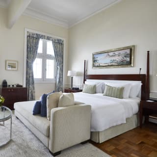 A large mahogany bed sits centre of a polished hardwood floor in a chic room with a chaise longue and mahogany side tables