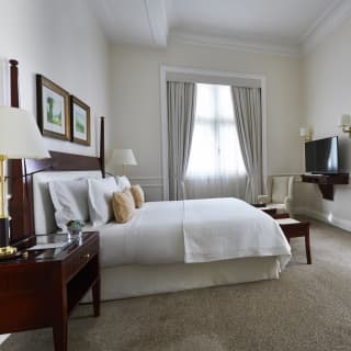 Full height windows allow in a soft light through voile curtains, illuminating a large room with deliciously crisp bed linens