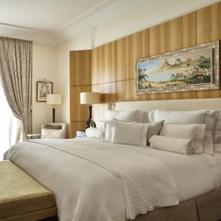 Dark glass lamps hold cream shades beside a king bed with white linens and pillows. A cream rug fills a polished wood floor