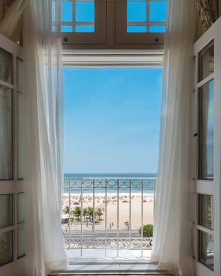 Billowing white voile curtains frame the oatmeal, cobalt, azure horizontal stripes that are the beach, sea and sky view