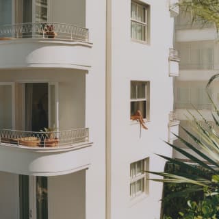 Legs dangle from an open first-floor window in a corner detail that shows Copacabana Palace's curve-edged art-deco balconies.