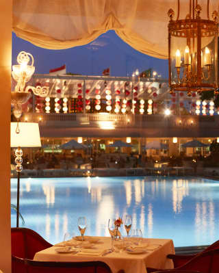 Diners enjoy the terrace as the night’s lights send shimmering reflections over the pool. Indoors, restaurant candles glow gold