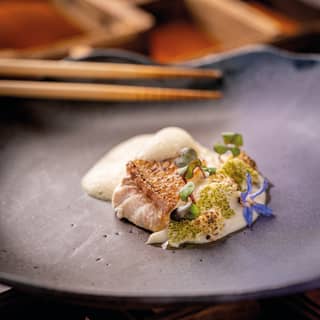 Close-up of a delicate starter of Suzuki Sakamushi with fish, presented on a black plate with chopsticks at Mee restaurant.