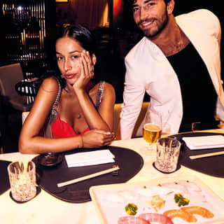 Three diners in casual evening dress sit at a table with chopsticks and a platter of chef’s selection sashimi