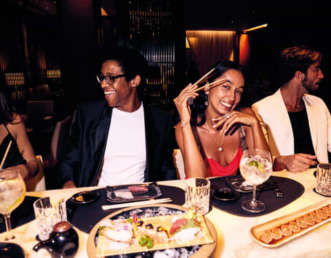 A woman smiling at the camera while holding chopsticks during a diner with friends at MEE restaurant