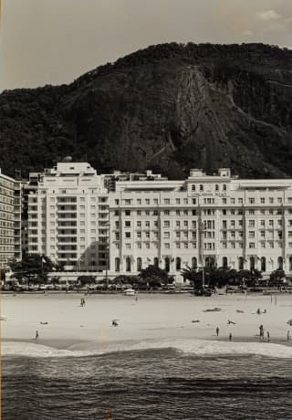 A vintage image of the hotel's facade and beach with the forested mountain behind shows almost no difference to today