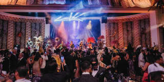A ballroom is in the mood to party, with samba dancers in feathered crowns, a live band and revellers in carnival masks