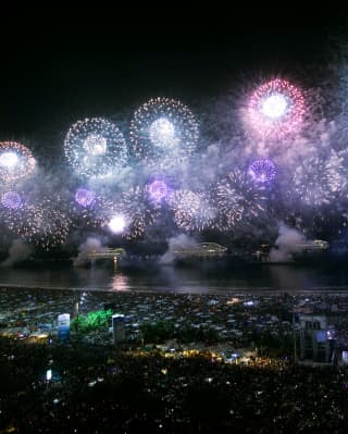 Pink, white and purple fireworks explode in bloom-like starbursts over Copacabana Beach after dark, during a celebration.