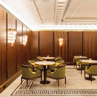 Greek-style edging on the marble floor and wooden framed velvet cocktail chairs nod towards art deco luxury styling