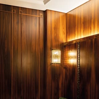 A velvet green bench hugs the length of a wood panelled wall. Art deco patterns are etched in the panels