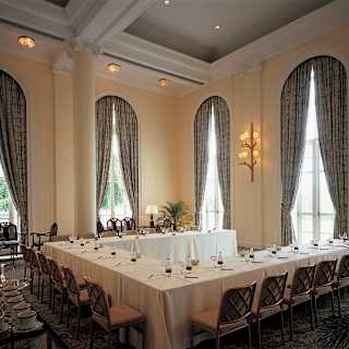 Meeting tables are set in a horseshoe shape with individual water and notepads. Cathedral height arched windows add drama