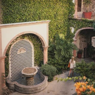 View over Casa Limón's courtyard with fountain alcove and ivy-clad walls, and the spires of Parroquial de San Miguel behind.