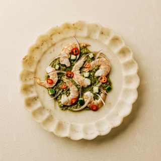 Prawn Aguachile with prawns on a lime and leaf base with red chillies, served on a scallop-edged plate, seen from above.