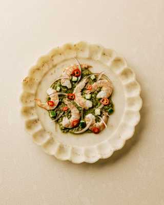 Prawn Aguachile with prawns on a lime and leaf base with red chillies, served on a scallop-edged plate, seen from above.