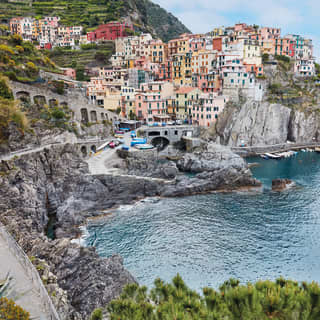 The tiny, picturesque Cinque Terre town of Manarola, with pastel buildings clinging to a rock above a small azure harbour.