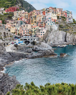 The tiny, picturesque Cinque Terre town of Manarola, with pastel buildings clinging to a rock above a small azure harbour.