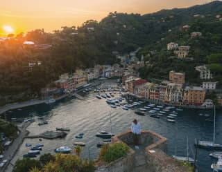 Man in a sunhat peering over the wall of a traditional fort towards Portofino piazzetta