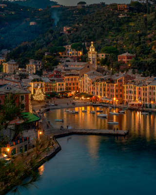 Portofino marina on a Christmas night, lined with glittering waterside restaurants casting reflections on the dark water.