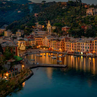 Portofino marina on a Christmas night, lined with glittering waterside restaurants casting reflections on the dark water.