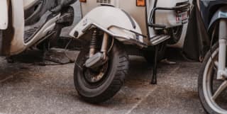 Close-up of a white Vespa scooter bearing the number five, parked in a row against a wall in a Tuscan street.