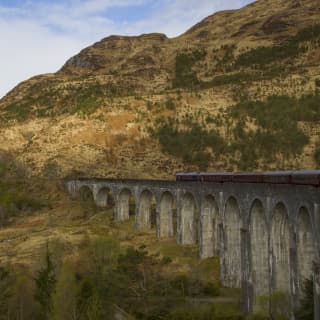 Burgundy train carriages on a stone arched viaduct over a grassy plain