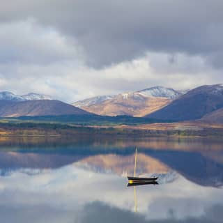 Small fishing boats floating on a mirror-still loch reflecting the snow-capped mountains