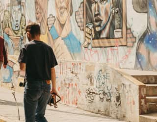 A man with a camera walks along a walled street in Barranco lined with graffiti and street-art portraits, seen from behind.