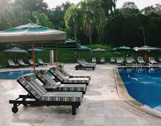View of multiple lounge chairs, shaded by parasols, circling two pools, one for paddling, the other for swimming.