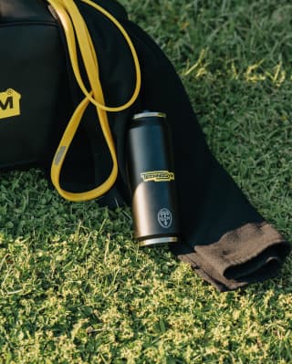 Close-up of a back kit bag with yellow ties and Technogym-branded water bottle lying on lawn.