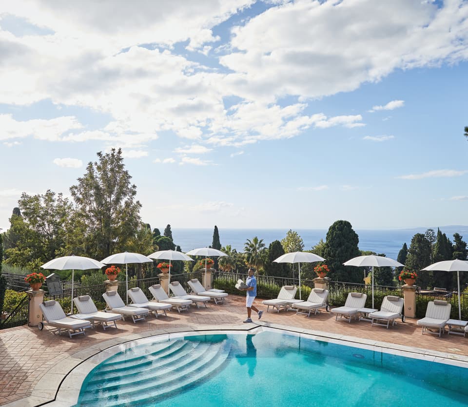 Pool man strolling beside an outdoor pool under sunny blue skies