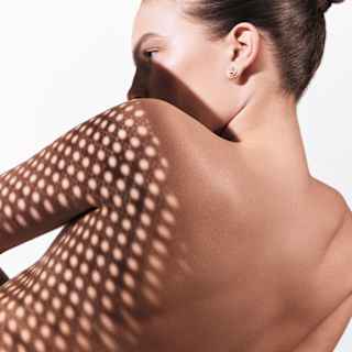 A pretty, dotted trellis shadow half-covers the bare back and shoulders of a woman in repose, seen from behind.
