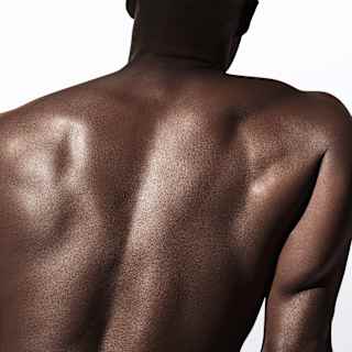 Close-up of the bare back of man with dark skin tone, glistening with oil treatment, seen from behind from neck to waist.