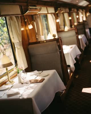 Angled view through the restaurant, where clothed window tables with glasses and cutlery are partitioned by high-back chairs.