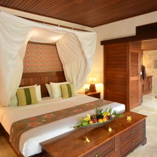 Linen canopy over a plush king-bed in a luxurious hotel room with teakwood details