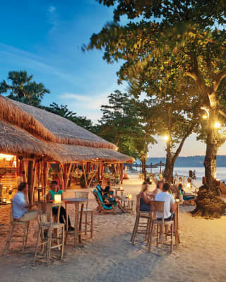 Open-air thatched beach hut bar on a white sandy Balinese beach at sunset