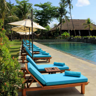 Poolside detail of wood and blue-cushioned loungers with white parasols in line by the cool waters of the large resort pool.